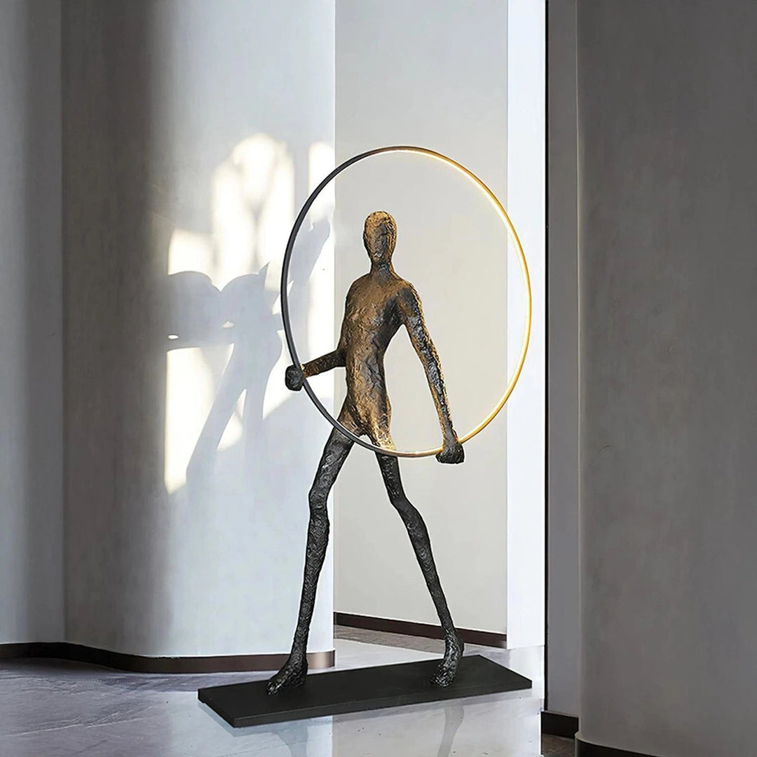 Modern bronze human figure sculpture holding a large circular hoop on a black base